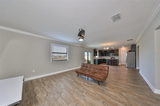 living room featuring ceiling fan with notable chandelier, a textured ceiling, light hardwood / wood-style floors, and ornamental molding