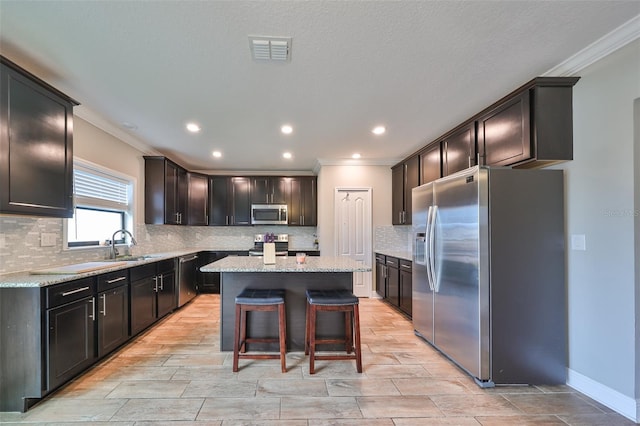 kitchen featuring a kitchen bar, light stone counters, ornamental molding, stainless steel appliances, and a kitchen island