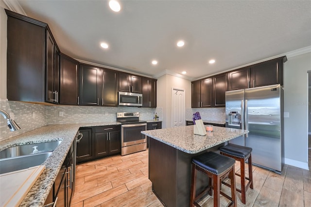 kitchen with crown molding, light stone countertops, appliances with stainless steel finishes, a kitchen island, and a kitchen bar