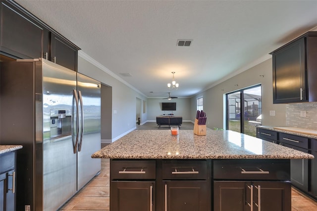 kitchen featuring stainless steel fridge, a kitchen island, light stone counters, and ceiling fan