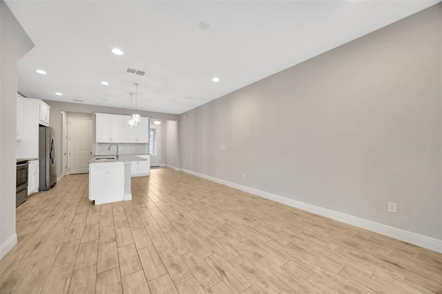 kitchen featuring sink, appliances with stainless steel finishes, white cabinetry, hanging light fixtures, and an island with sink