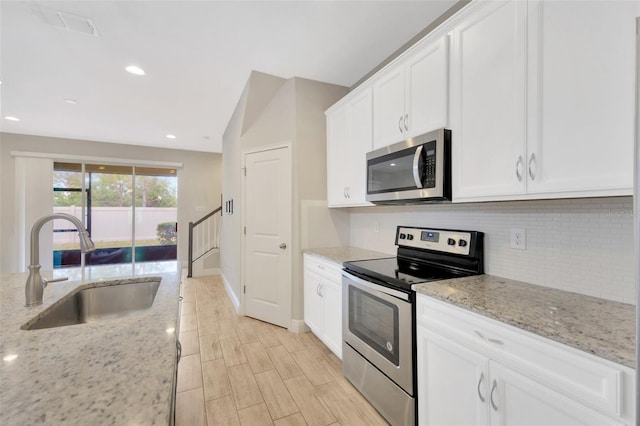 kitchen with sink, appliances with stainless steel finishes, backsplash, light stone counters, and white cabinets