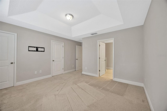 unfurnished bedroom featuring light colored carpet and a tray ceiling