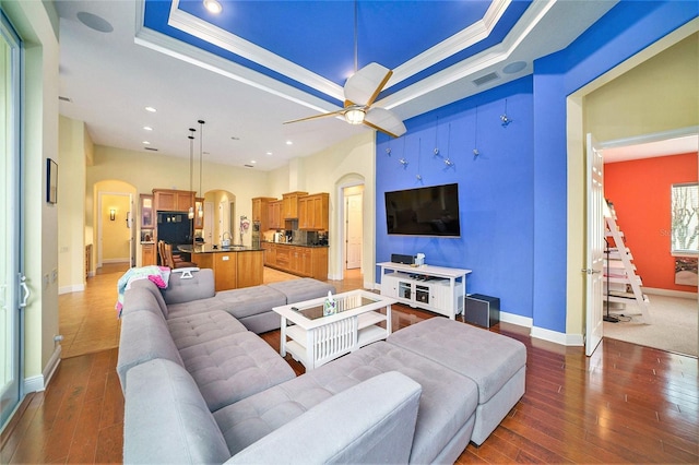 living room with ceiling fan, a raised ceiling, ornamental molding, and dark hardwood / wood-style flooring