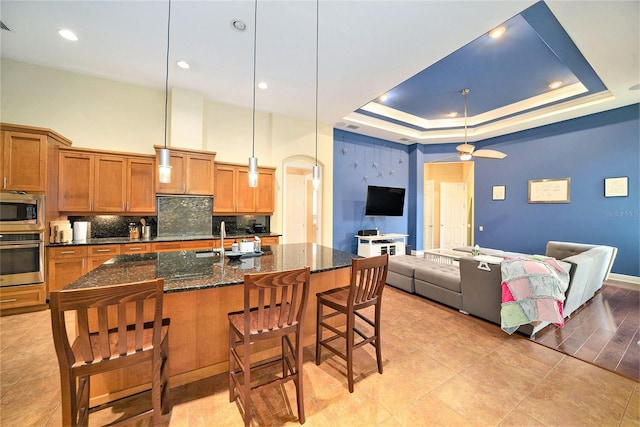 kitchen featuring decorative light fixtures, a spacious island, appliances with stainless steel finishes, and a tray ceiling