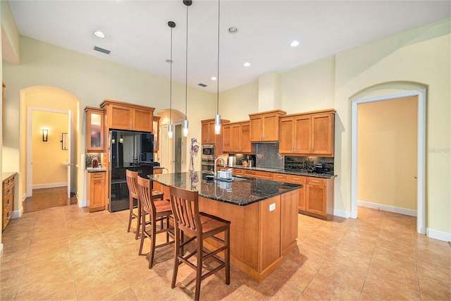 kitchen featuring decorative light fixtures, sink, tasteful backsplash, a kitchen island with sink, and black fridge