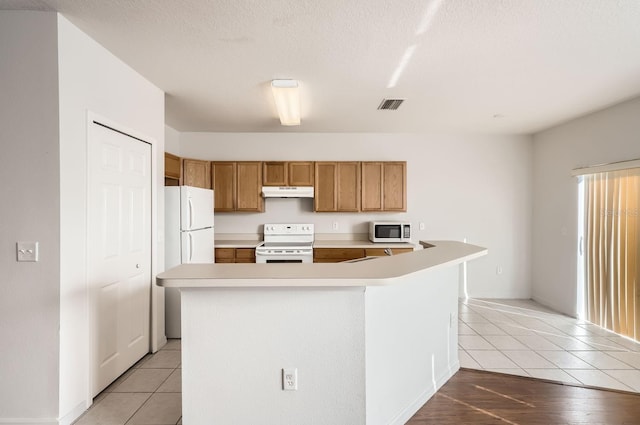 kitchen featuring a center island with sink, white appliances, a textured ceiling, and light tile patterned floors