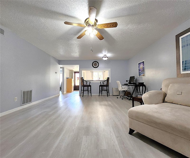 living room with ceiling fan, light hardwood / wood-style flooring, and a textured ceiling