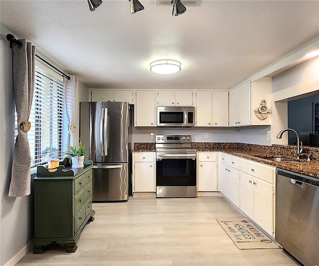 kitchen featuring sink, light hardwood / wood-style flooring, white cabinetry, dark stone countertops, and stainless steel appliances