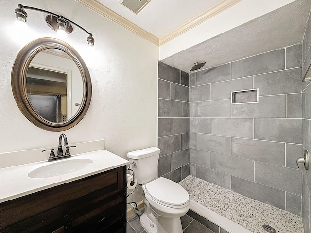 bathroom with toilet, a tile shower, tile patterned flooring, crown molding, and vanity