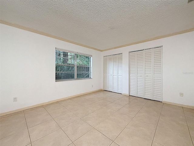 unfurnished bedroom featuring light tile patterned floors, crown molding, a textured ceiling, and two closets