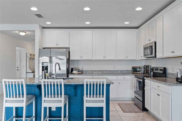 kitchen with white cabinets, light stone counters, stainless steel appliances, and an island with sink