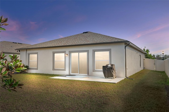 back house at dusk featuring a patio and a lawn