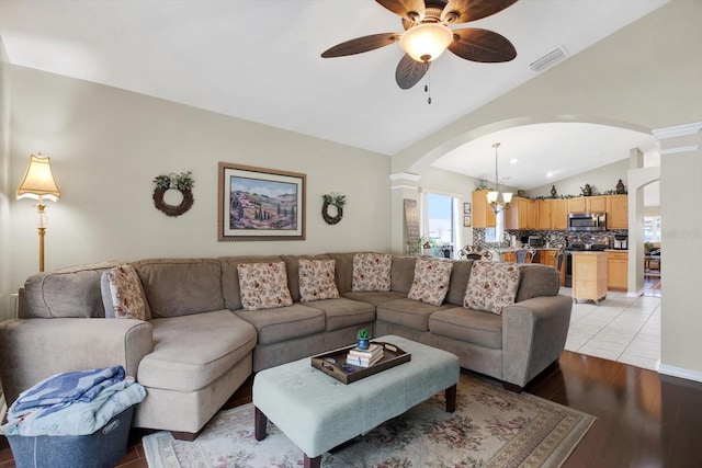 living room with ceiling fan with notable chandelier, light hardwood / wood-style floors, and vaulted ceiling