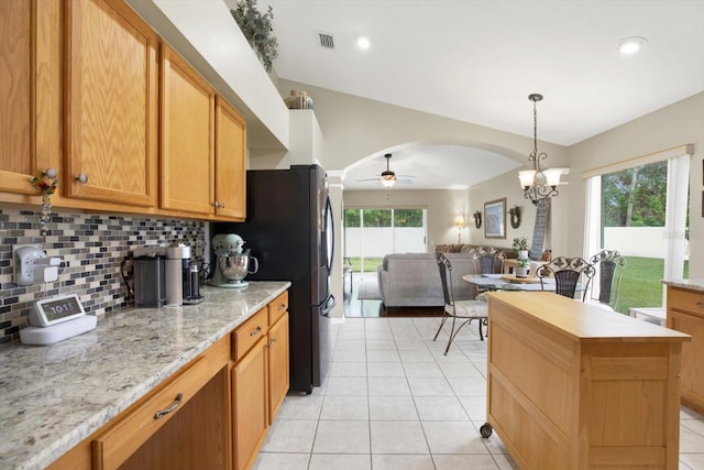 kitchen featuring ceiling fan with notable chandelier, decorative backsplash, a kitchen island, light tile patterned flooring, and light stone counters