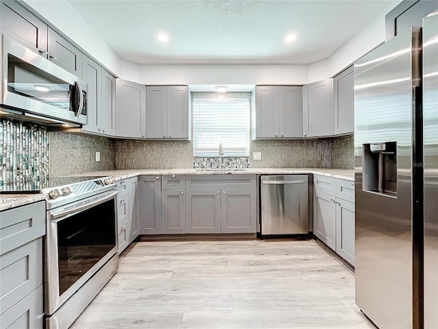 kitchen with gray cabinetry, sink, stainless steel appliances, light stone counters, and backsplash