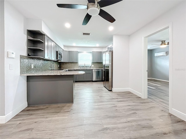 kitchen with a wall mounted AC, tasteful backsplash, light hardwood / wood-style floors, kitchen peninsula, and stainless steel appliances