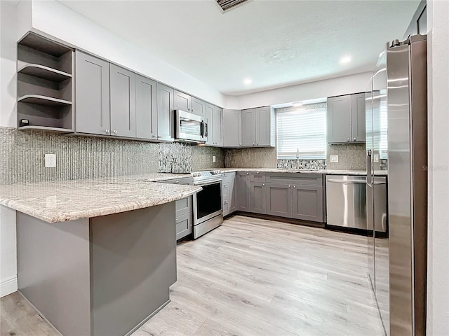 kitchen with kitchen peninsula, stainless steel appliances, light stone counters, and light hardwood / wood-style floors