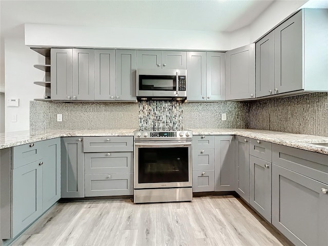 kitchen with backsplash, gray cabinetry, light stone counters, and appliances with stainless steel finishes