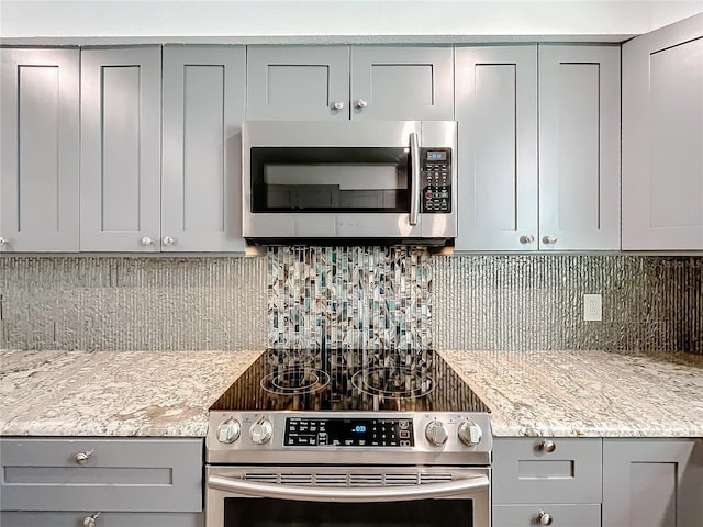 kitchen featuring light stone countertops, stainless steel appliances, tasteful backsplash, and gray cabinetry