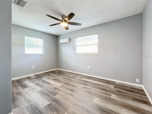 unfurnished room featuring a textured ceiling, hardwood / wood-style flooring, an AC wall unit, and a healthy amount of sunlight