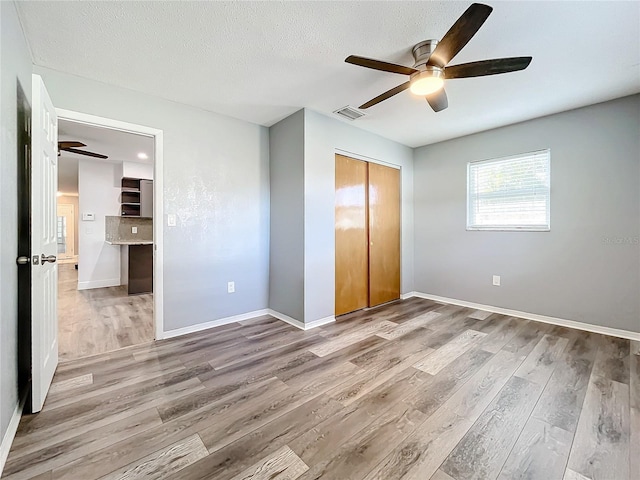 unfurnished bedroom featuring ceiling fan, light hardwood / wood-style floors, a textured ceiling, and a closet