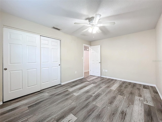 unfurnished bedroom with ceiling fan, a closet, hardwood / wood-style floors, and a textured ceiling