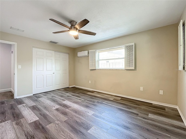 unfurnished bedroom featuring a wall mounted AC, a closet, dark hardwood / wood-style floors, and ceiling fan