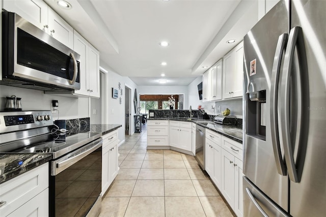 kitchen with dark stone counters, light tile patterned floors, white cabinetry, kitchen peninsula, and stainless steel appliances