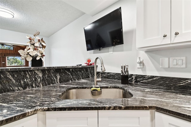 interior space featuring white cabinetry, sink, dark stone counters, and a textured ceiling