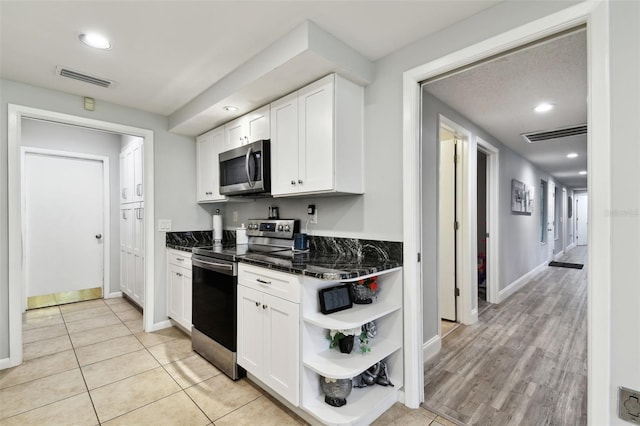 kitchen featuring light tile patterned flooring, dark stone countertops, white cabinetry, and appliances with stainless steel finishes