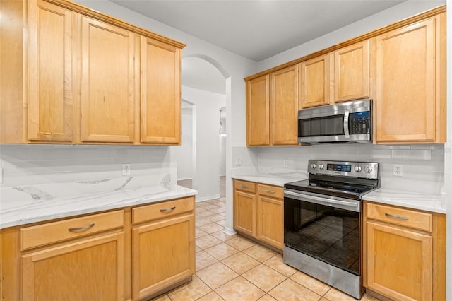 kitchen featuring light stone countertops, appliances with stainless steel finishes, decorative backsplash, light brown cabinetry, and light tile patterned floors