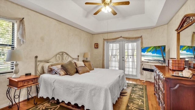 bedroom with french doors, a raised ceiling, hardwood / wood-style flooring, ceiling fan, and access to exterior