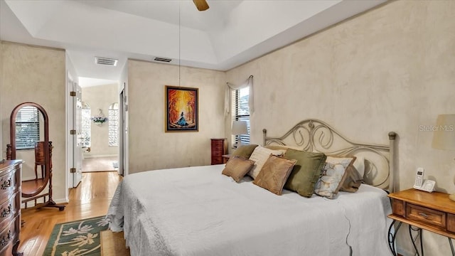 bedroom with connected bathroom, a raised ceiling, ceiling fan, and light wood-type flooring