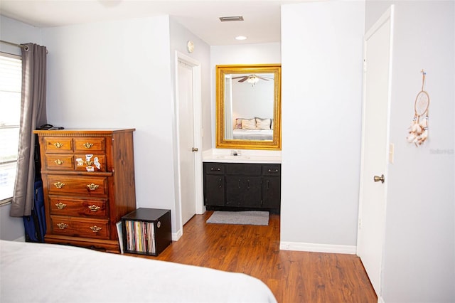 bedroom with baseboards, wood finished floors, visible vents, and a sink