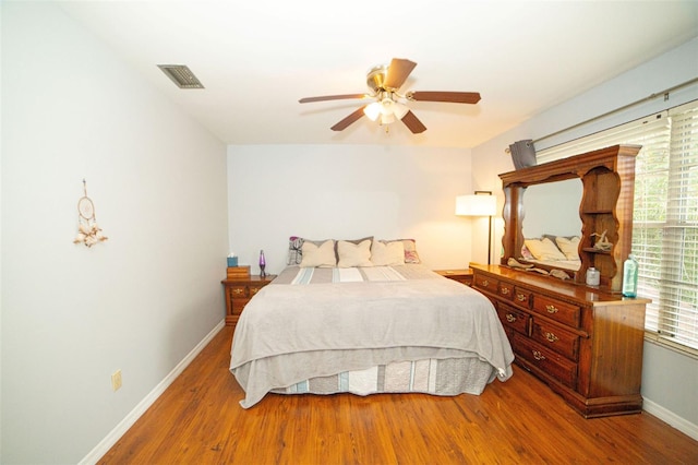 bedroom with ceiling fan, wood finished floors, visible vents, and baseboards