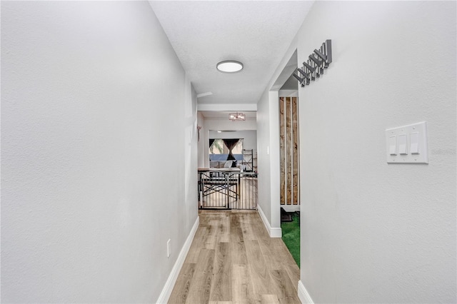 corridor with a textured ceiling and light hardwood / wood-style flooring