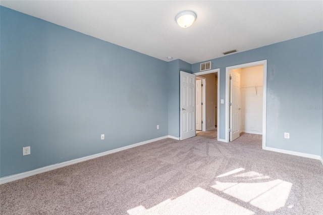 unfurnished bedroom with a spacious closet, a closet, and carpet