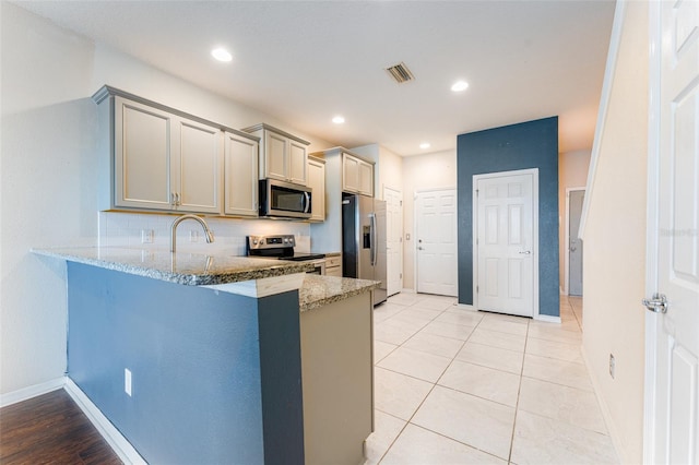 kitchen with kitchen peninsula, a kitchen bar, light stone countertops, gray cabinetry, and stainless steel appliances