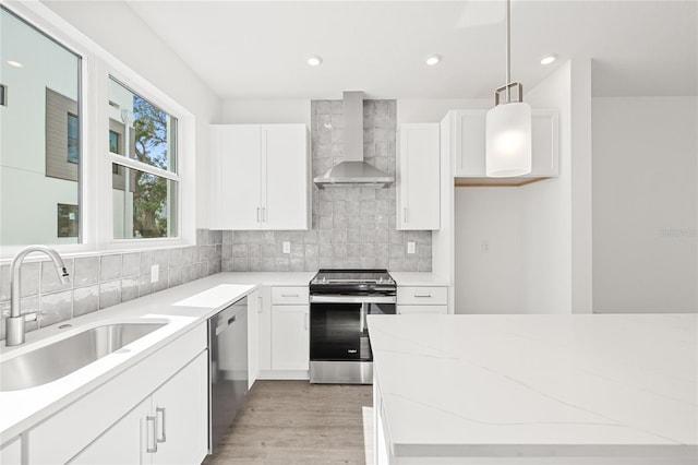 kitchen featuring pendant lighting, stainless steel appliances, white cabinetry, and wall chimney range hood