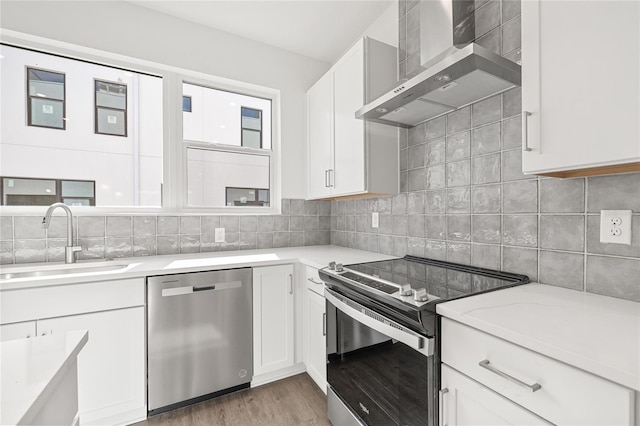 kitchen featuring white cabinets, sink, wall chimney exhaust hood, light stone counters, and stainless steel appliances