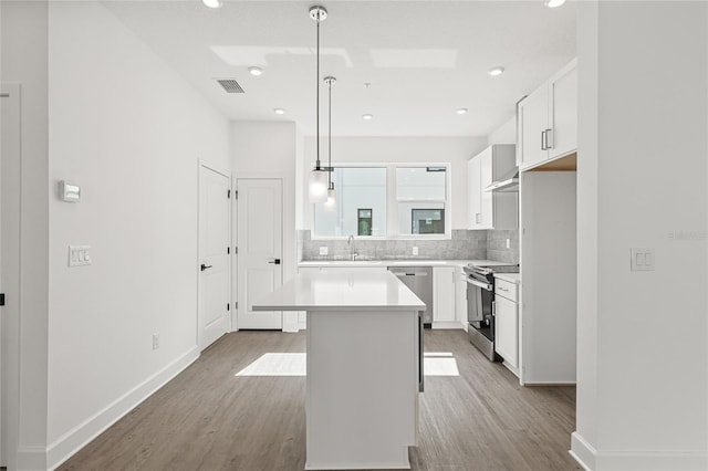 kitchen with appliances with stainless steel finishes, white cabinets, a center island, light hardwood / wood-style floors, and hanging light fixtures