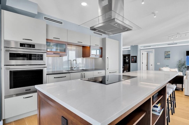 kitchen with sink, a center island, double oven, island exhaust hood, and white cabinets