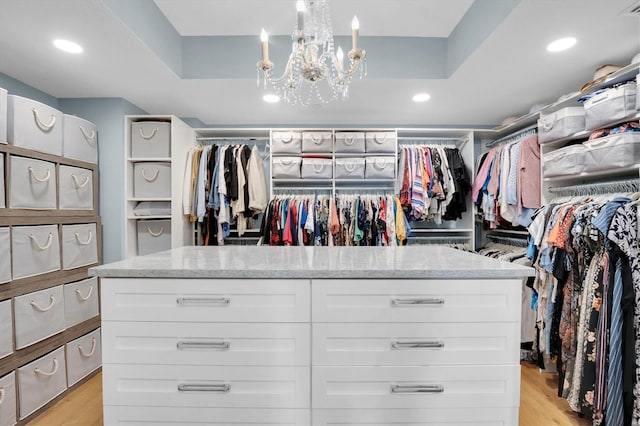 walk in closet with a raised ceiling, light hardwood / wood-style floors, and a notable chandelier