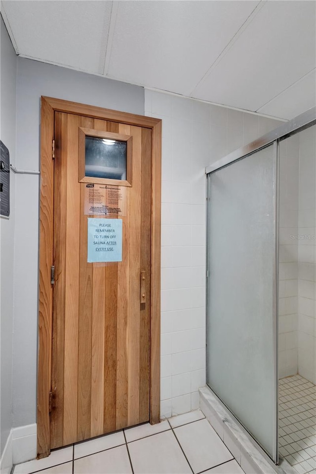 interior space featuring tile patterned flooring, a shower with shower door, and wooden walls