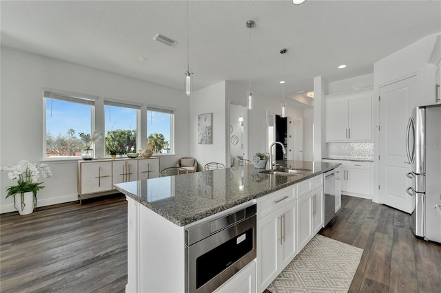 kitchen with a kitchen island with sink, sink, pendant lighting, and appliances with stainless steel finishes