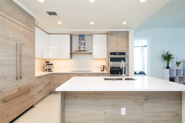 kitchen featuring stovetop, stainless steel double oven, a center island with sink, and white cabinetry