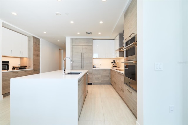 kitchen with wall chimney exhaust hood, a kitchen island with sink, sink, light tile patterned floors, and white cabinetry