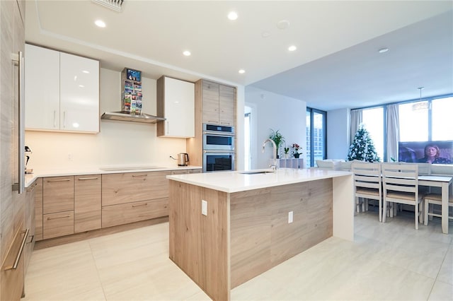 kitchen with sink, stainless steel double oven, cooktop, a center island with sink, and white cabinets