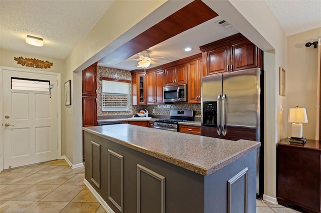 kitchen with ceiling fan, appliances with stainless steel finishes, light tile patterned flooring, and a kitchen island